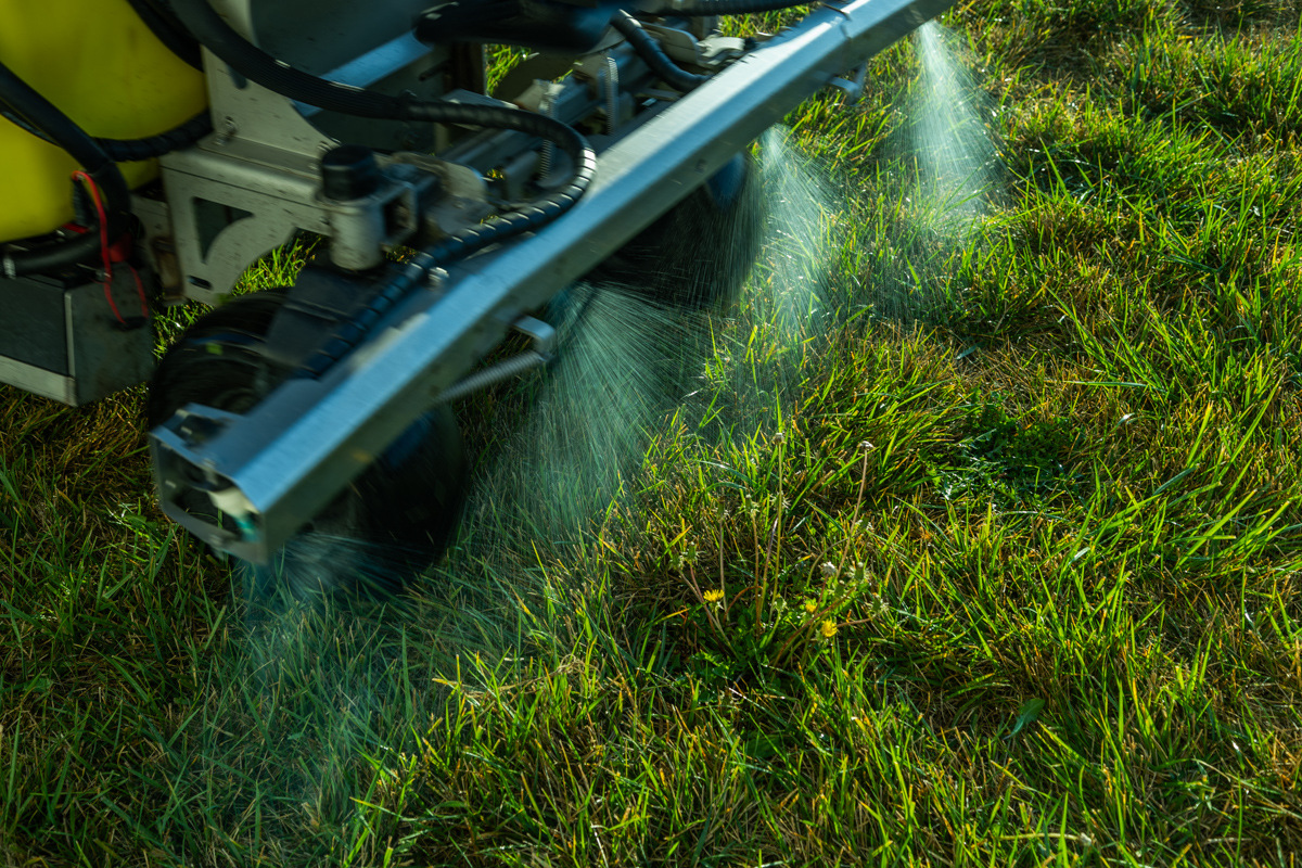 Close-up of a sprayer boom misting liquid weed control onto grass