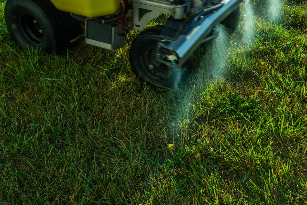 Liquid treatment misting from a sprayer nozzle beside the machine's wheel