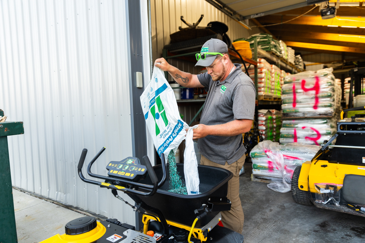 Technician pouring a bag of granular fertilizer into a spreader inside the shop