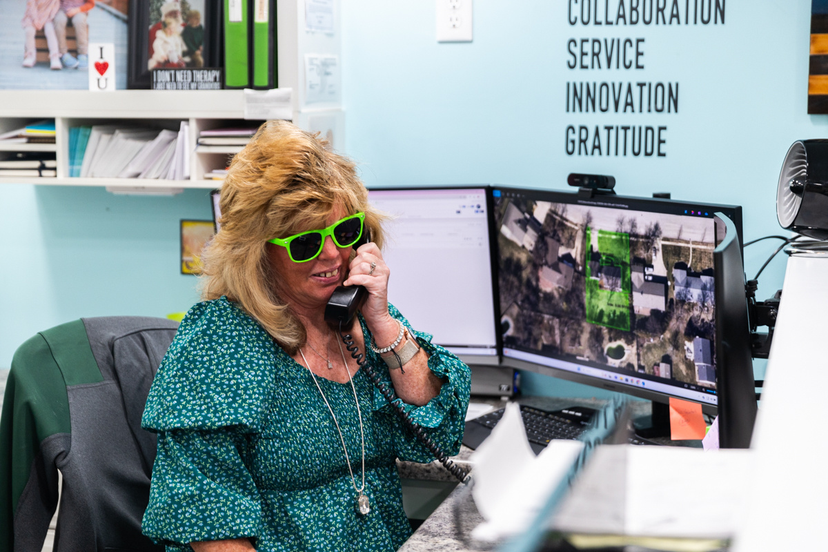 Office team member in green sunglasses on the phone below a wall reading Collaboration, Service, Innovation, Gratitude