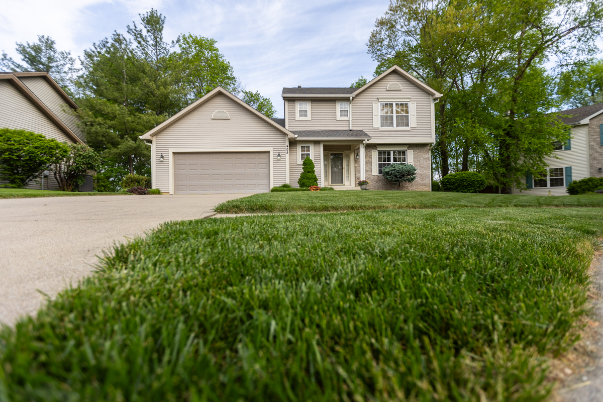Low view across a thick front lawn toward a two-story home and its driveway