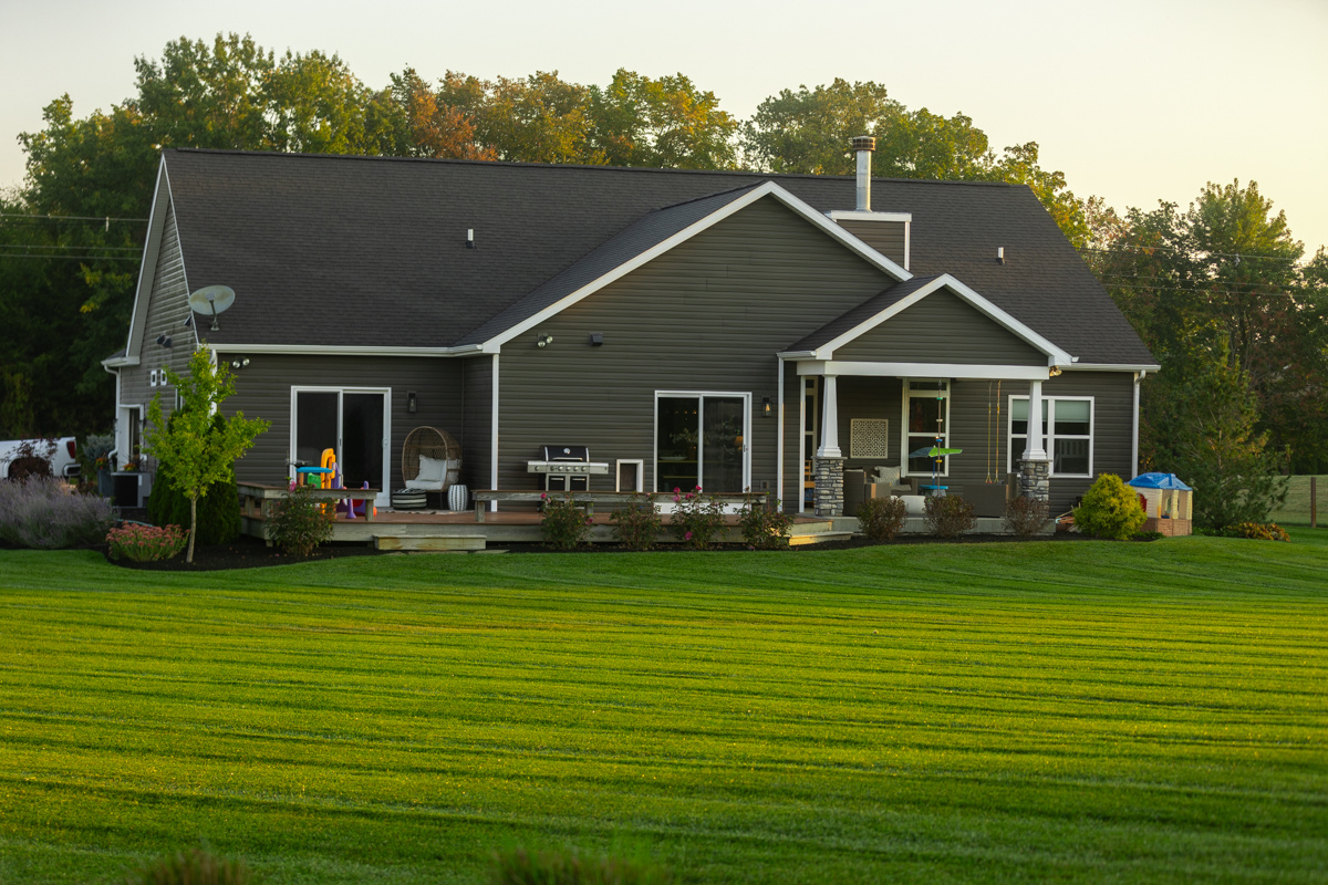 Gray-sided home with a wide, striped back lawn in evening light