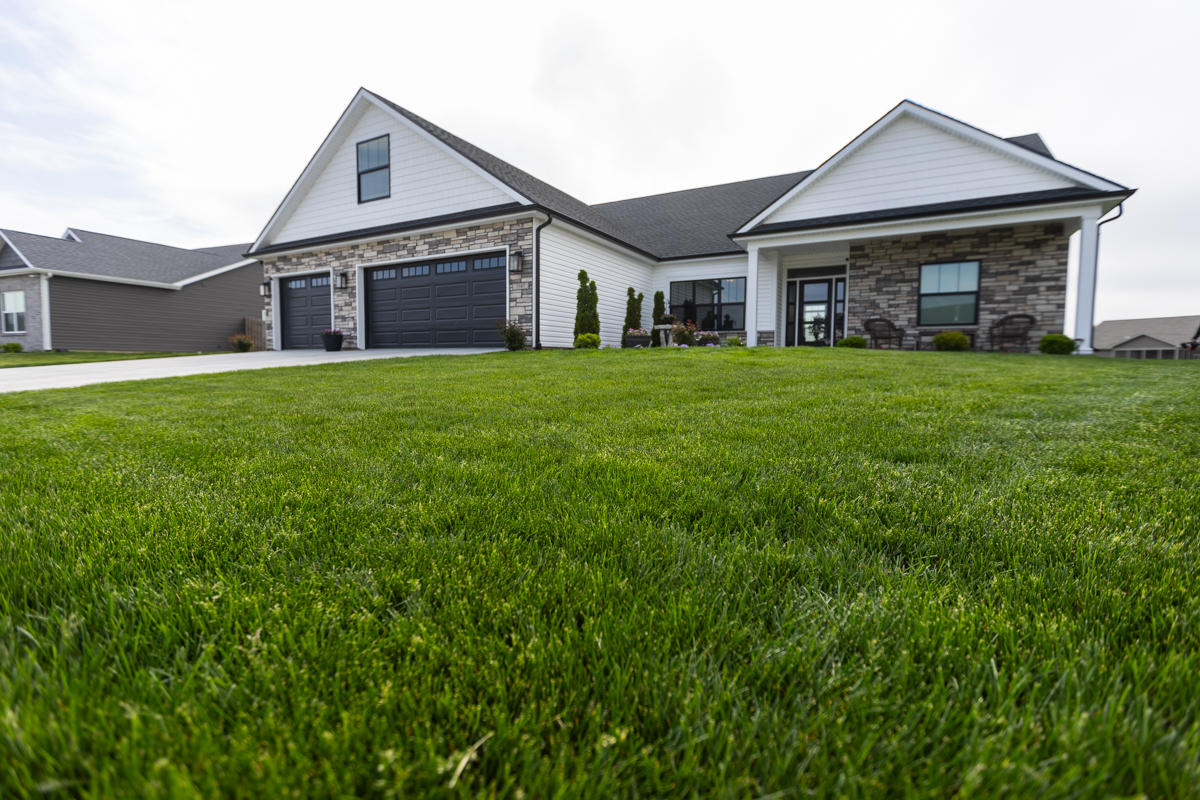 Thick front lawn of a white and stone ranch home with a two-car garage