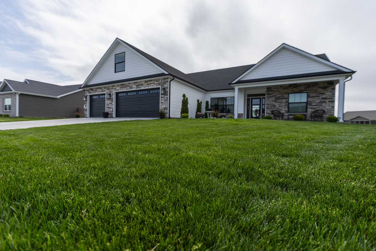 Green front lawn of a white ranch home with stone accents under a cloudy sky