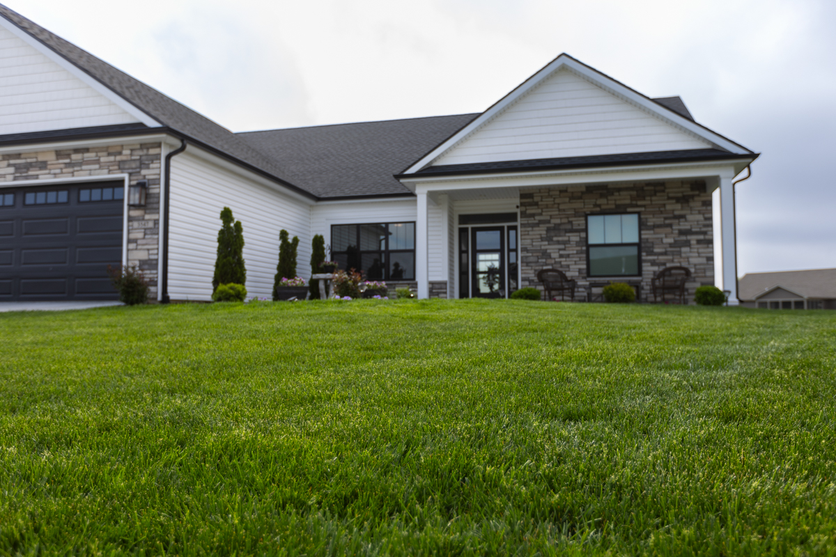 Green lawn in front of a white farmhouse-style home with a stone porch
