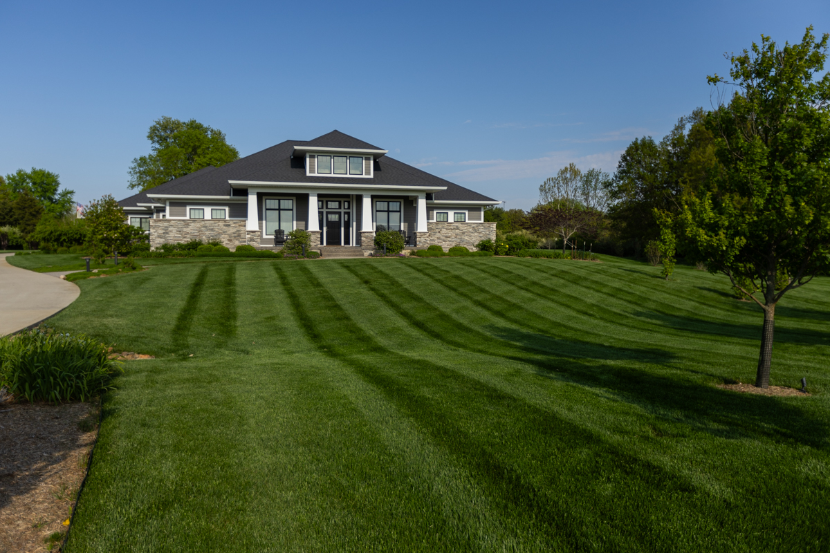Long, striped lawn leading up to a large stone and shingle home