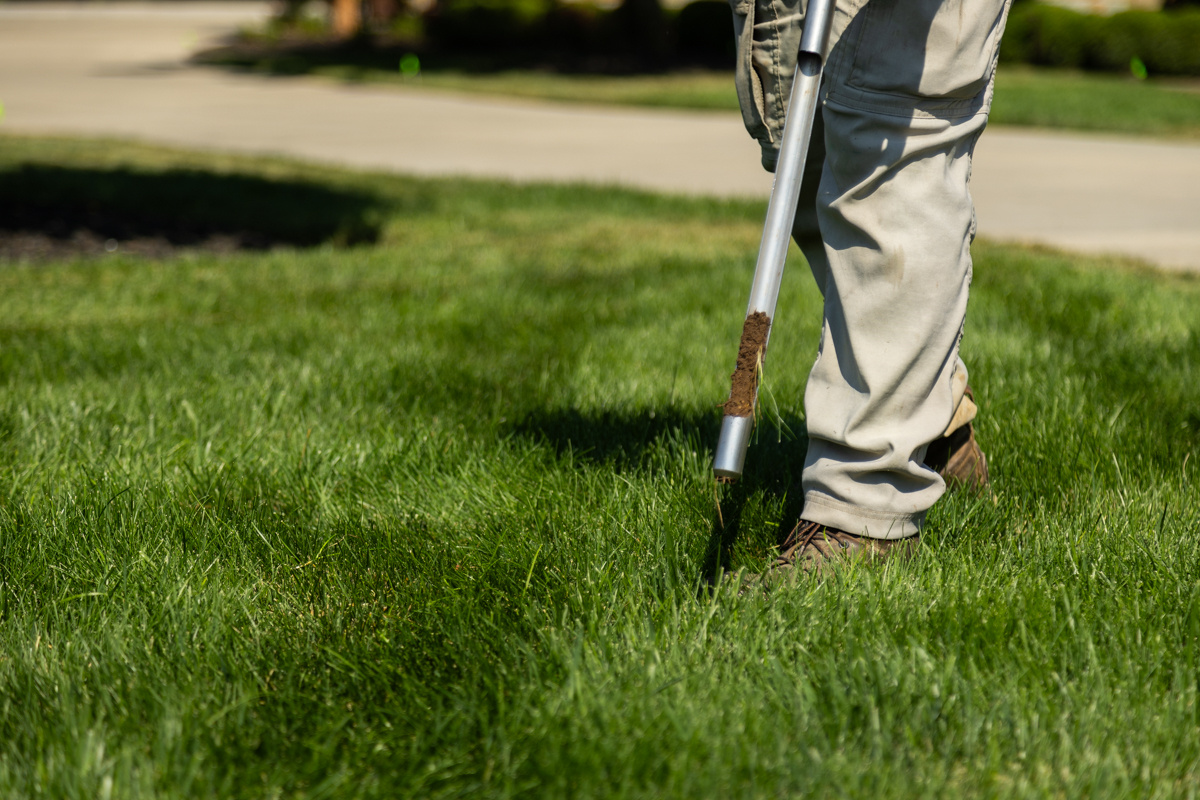Soil probe holding a fresh core sample, beside a technician standing on a lawn