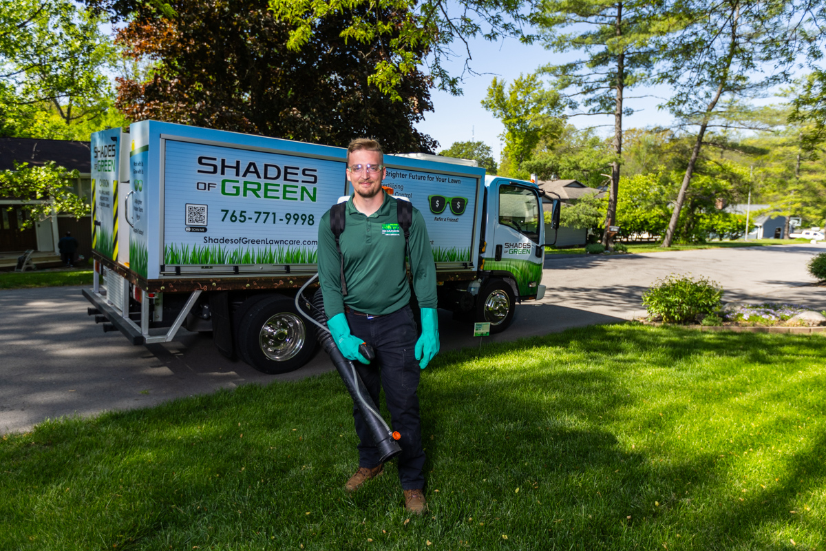 Mosquito control technician with a backpack sprayer in front of a Shades of Green truck