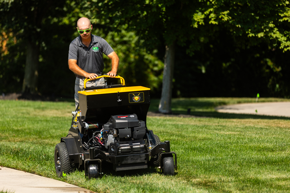 Technician steering a stand-on aerator across a shaded lawn