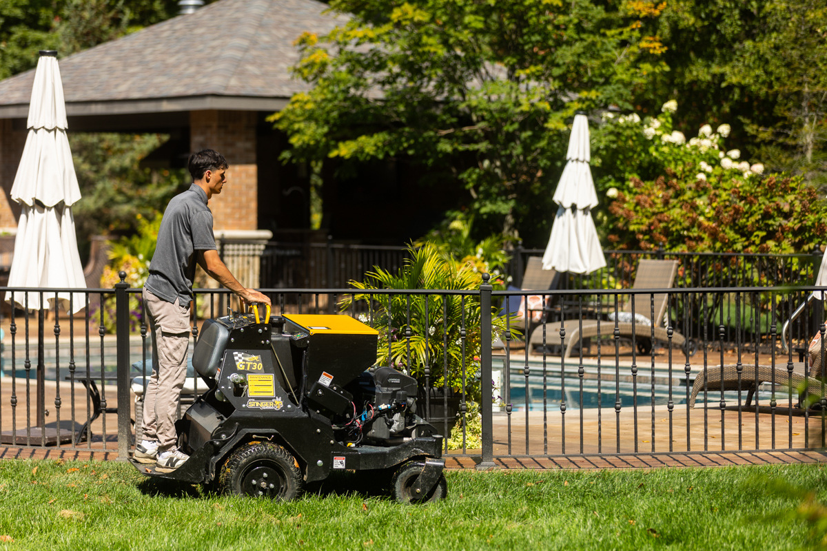 Technician running a stand-on aerator past a fenced backyard pool