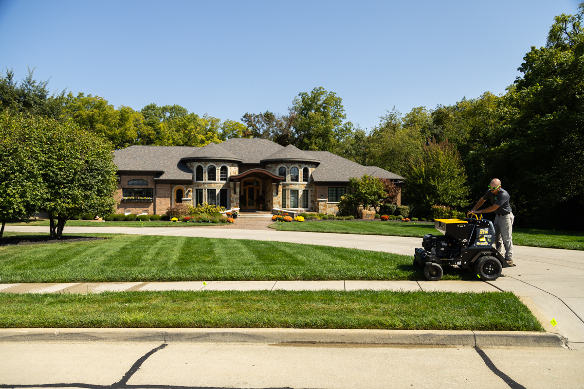Technician aerating a striped front lawn outside a large stone home
