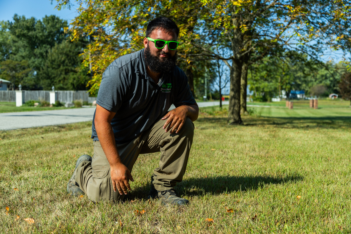 Technician kneeling to inspect a thin, struggling lawn
