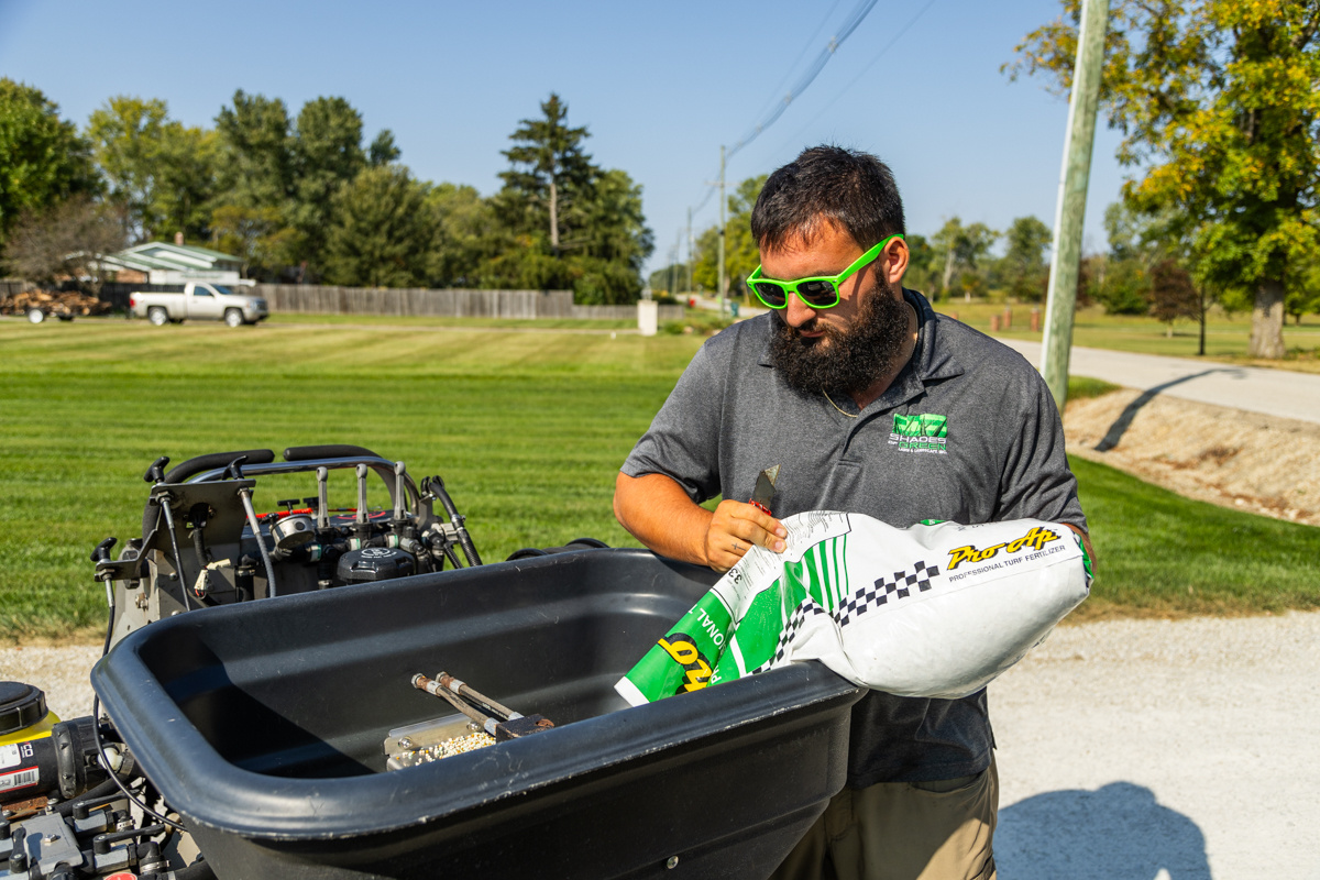 Technician in green sunglasses pouring granular fertilizer into a spreader hopper