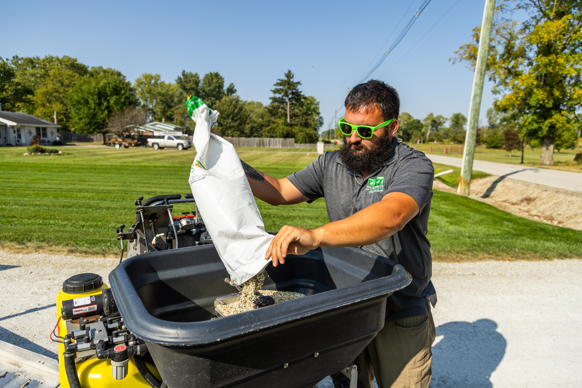 Technician emptying a bag of granular fertilizer into a ride-on spreader's hopper