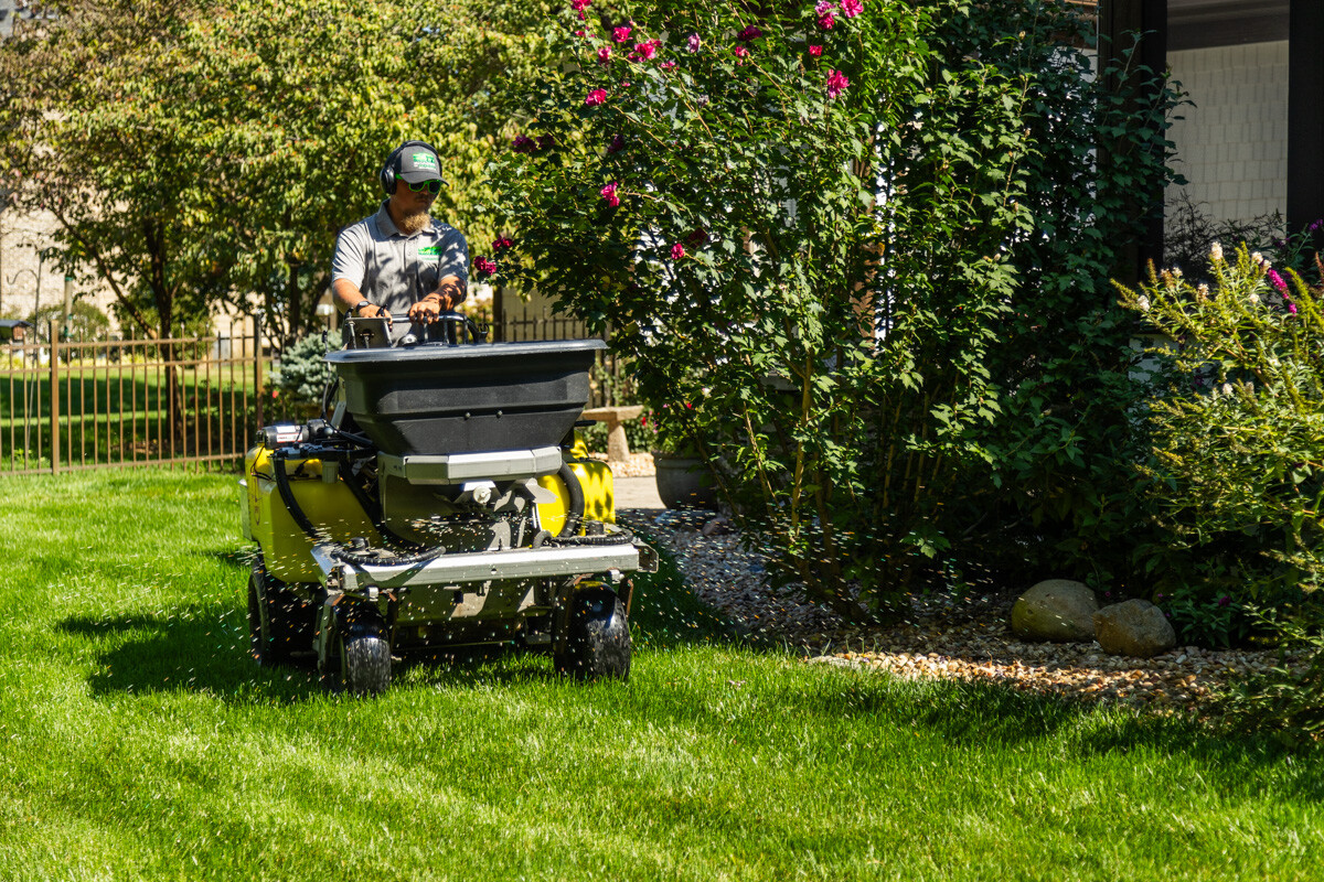Technician on a ride-on spreader applying granular fertilizer in a landscaped backyard