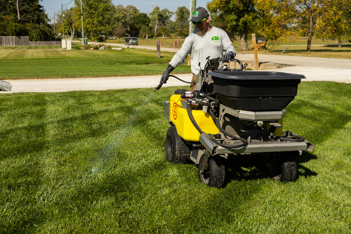 Technician on a ride-on sprayer spot-treating a lawn with a hose wand