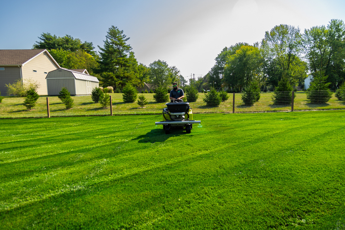 Technician on a ride-on machine far across a wide, striped backyard lawn