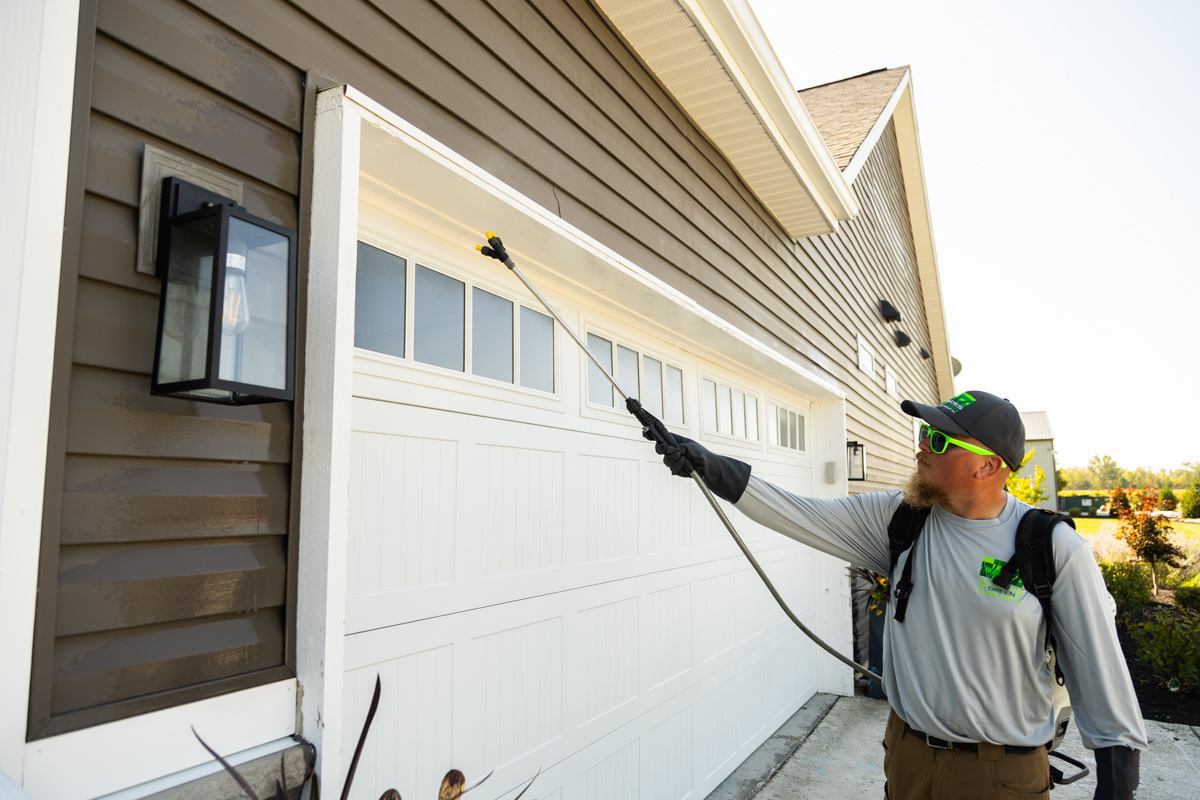 Technician spraying a perimeter pest treatment along a garage door frame