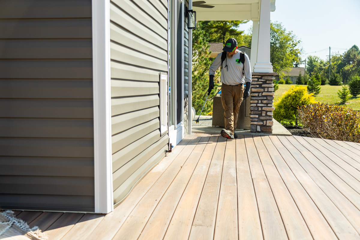 Technician walking a home's front porch with a pest control sprayer