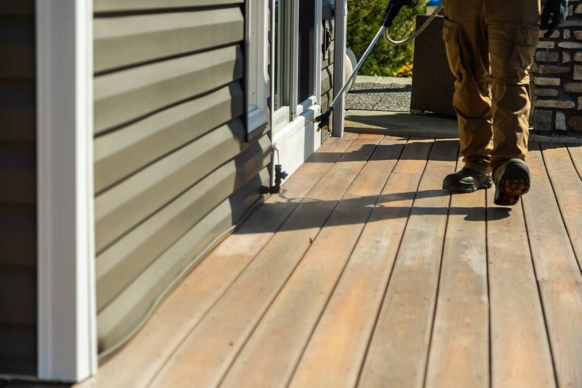 Technician spraying along the base of a home's siding on a front porch