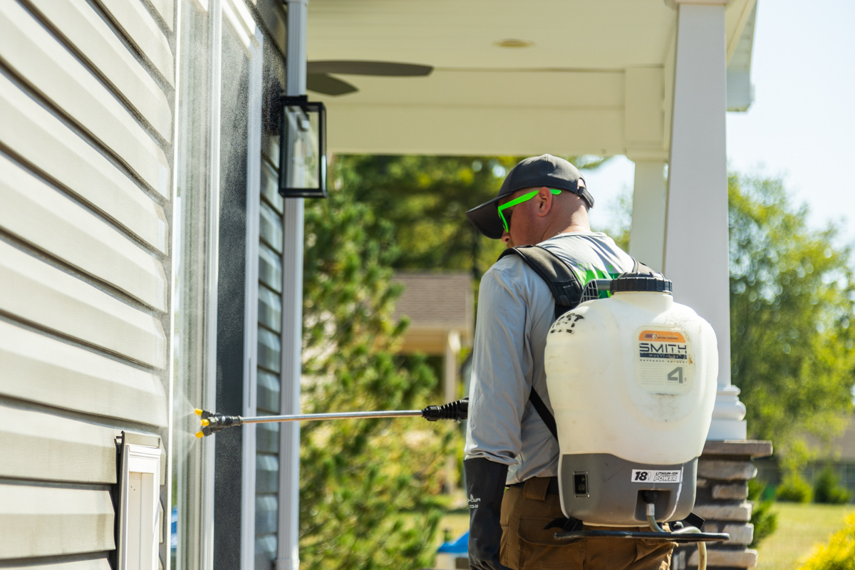 Technician with a backpack sprayer treating a window frame on a home's porch