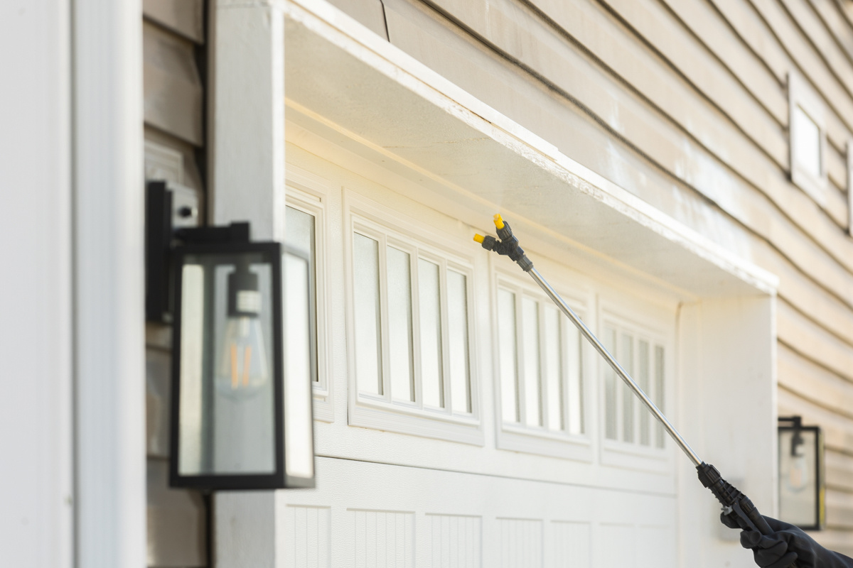 Close-up of a spray wand treating the top of a garage door frame