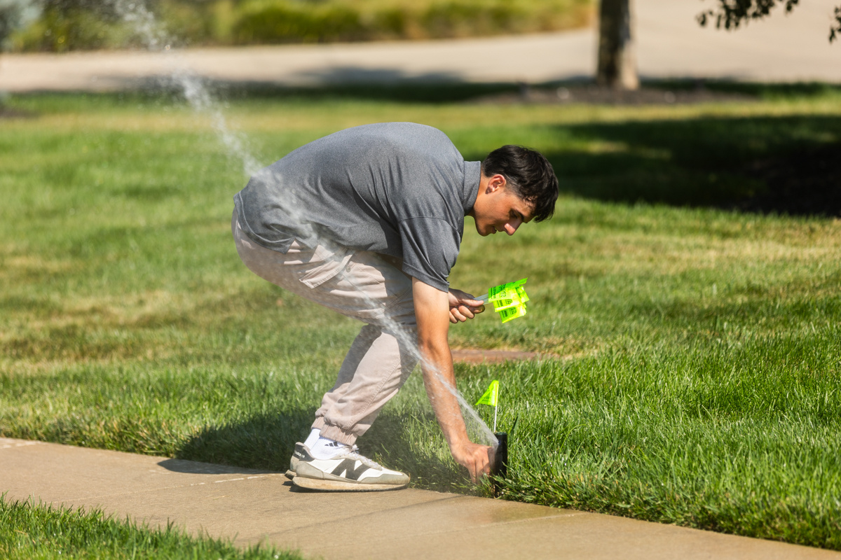 Technician placing a marker flag beside a running sprinkler head at the lawn's edge