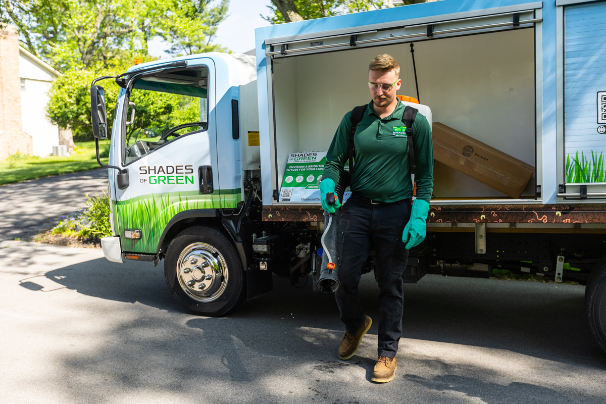 Technician with a backpack sprayer stepping away from a Shades of Green box truck